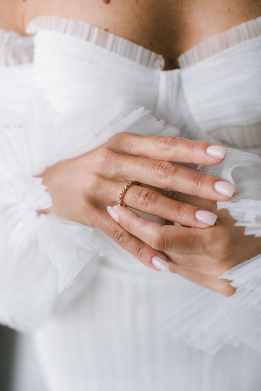 Dettaglio delle mani della sposa incrociate sul petto con anello a fede ornata di pietre, manica di tulle a balze